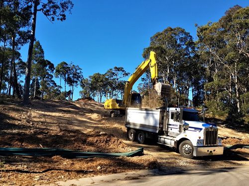 A yellow excavator is loading dirt into a dump truck.