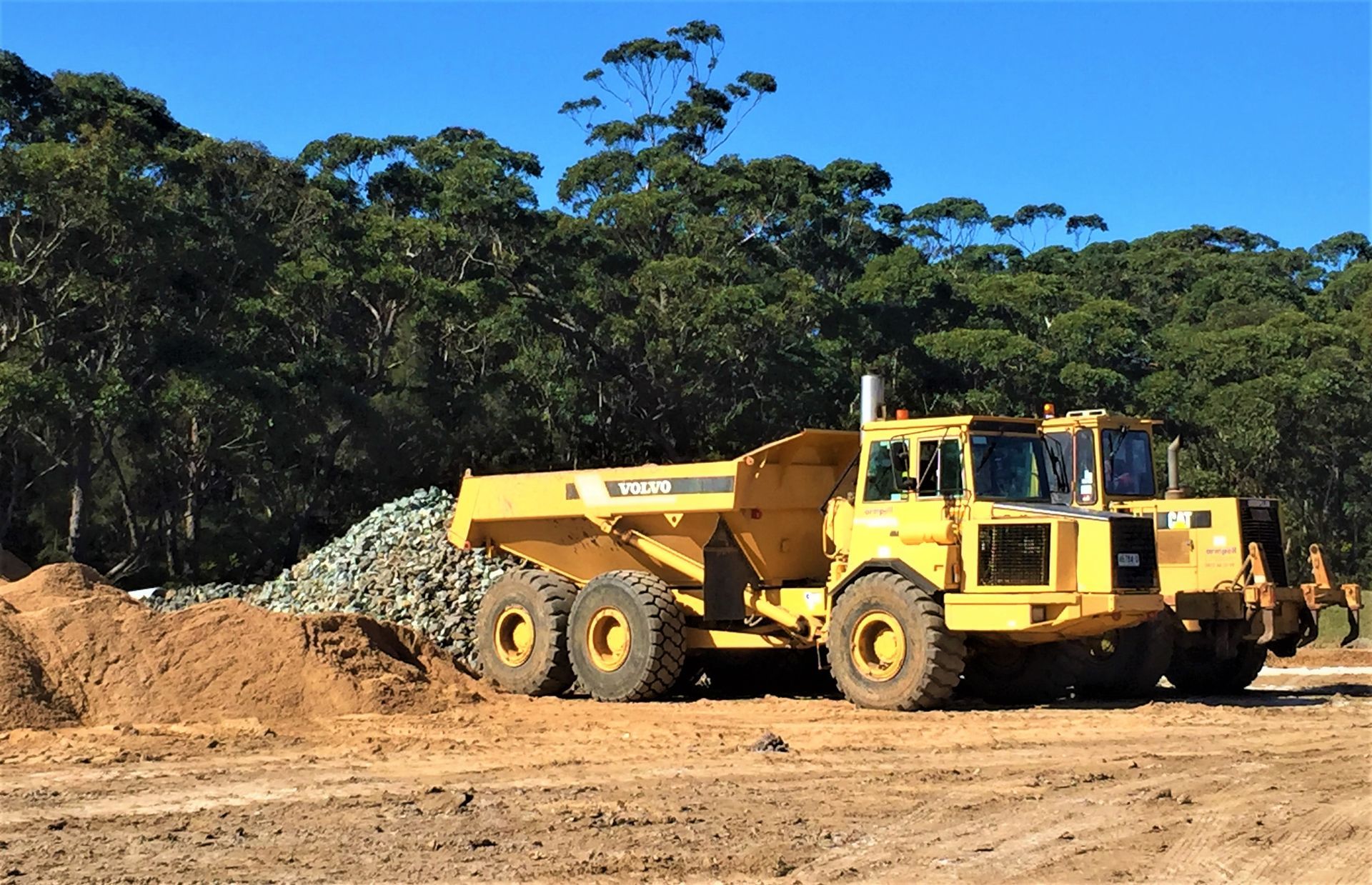 A yellow dump truck is sitting on top of a dirt field.