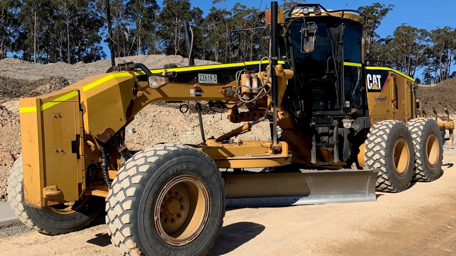 A yellow and black caterpillar grader is parked on a dirt road.