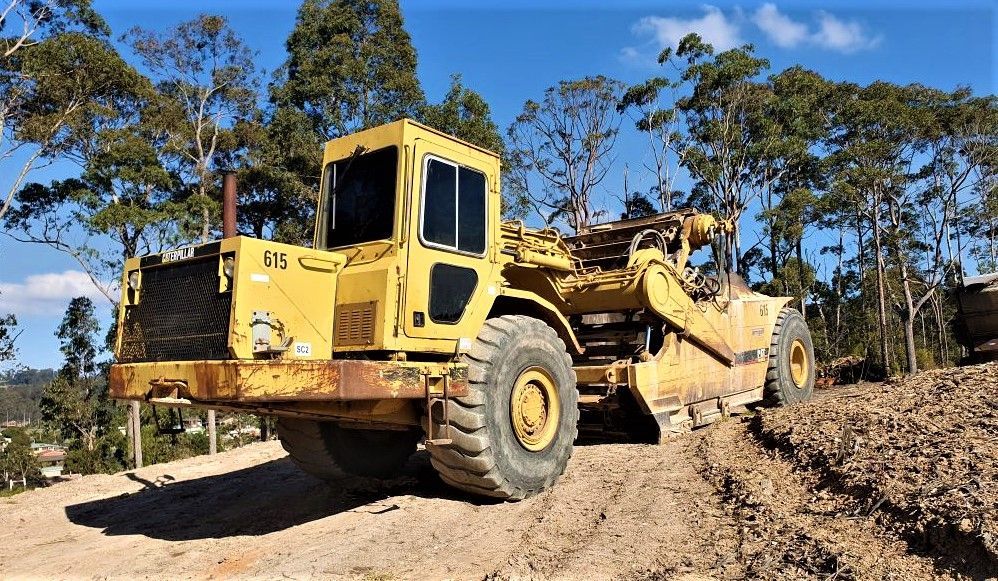 A yellow tractor is parked on the side of a dirt road.