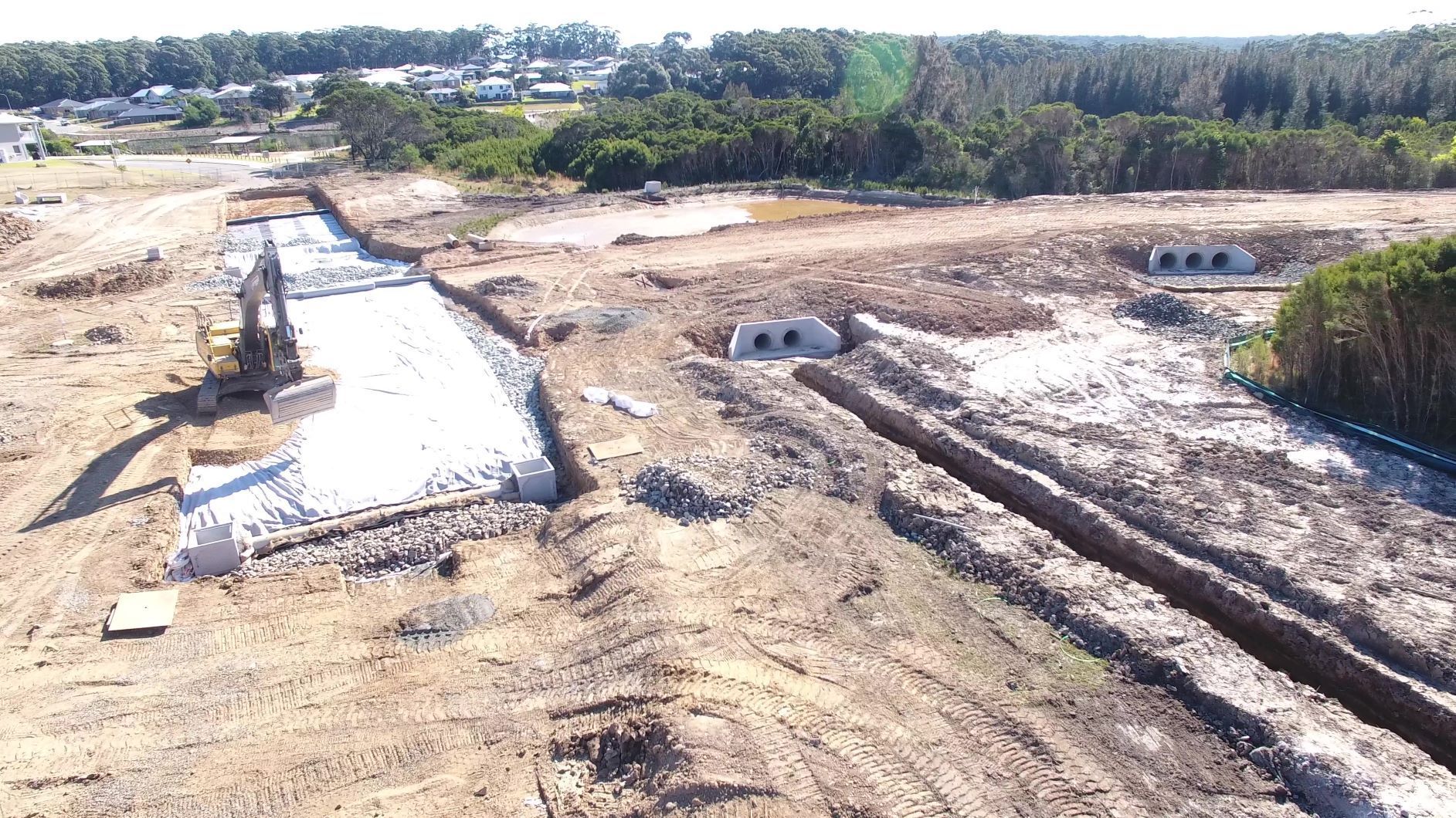 An aerial view of a construction site with a lot of dirt and trees in the background.
