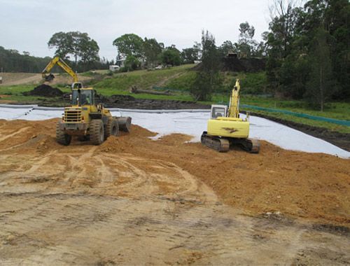Two construction vehicles are working on a dirt field.