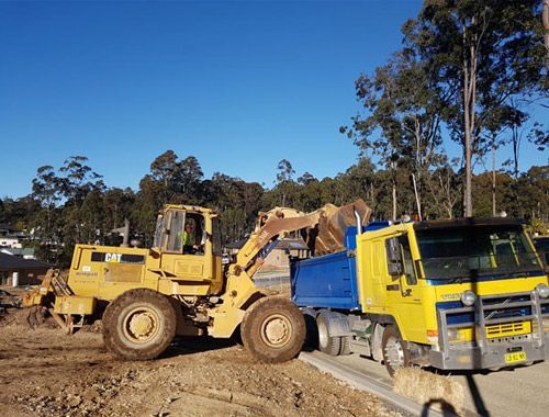 A bulldozer is loading dirt into a dump truck.