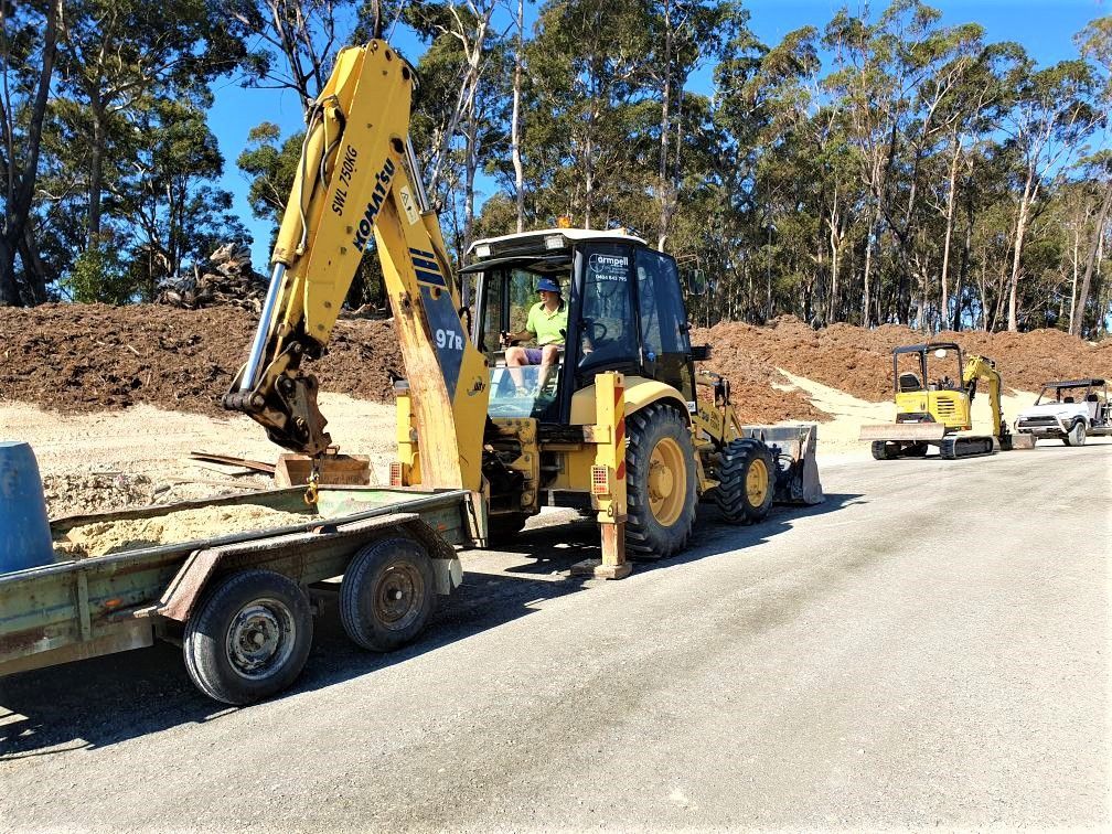 A man is driving a yellow excavator on a trailer.