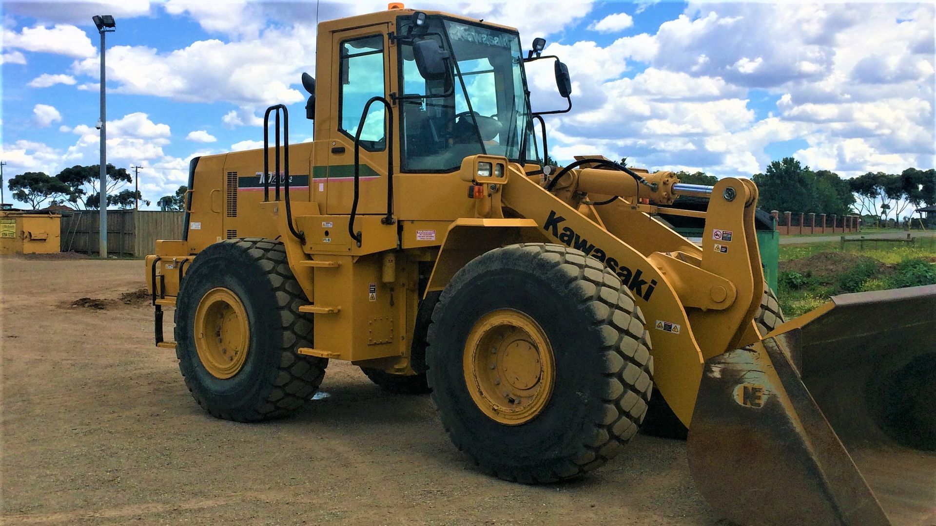 A yellow kawasaki wheel loader is parked in a dirt lot.