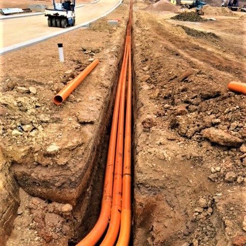 A bunch of orange pipes are laying in the dirt