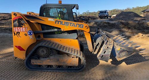 A mustang bulldozer is sitting on top of a dirt field.