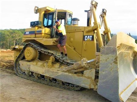 A man is standing on the side of a cat bulldozer.
