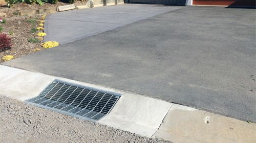 A drain on the side of a road next to a driveway