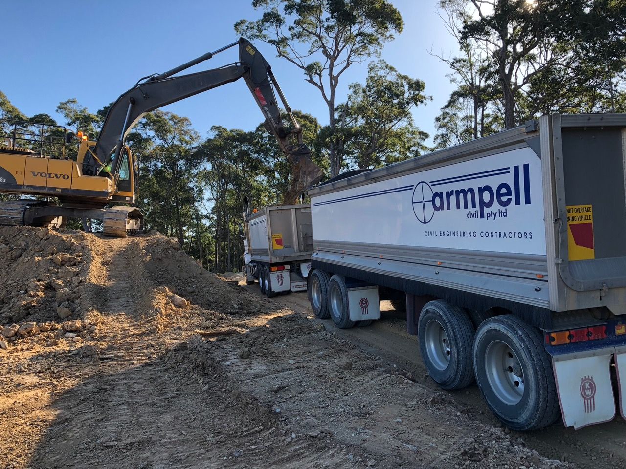 A dump truck is being loaded with dirt by an excavator.