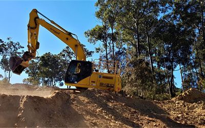 A yellow excavator is working on a dirt hill.