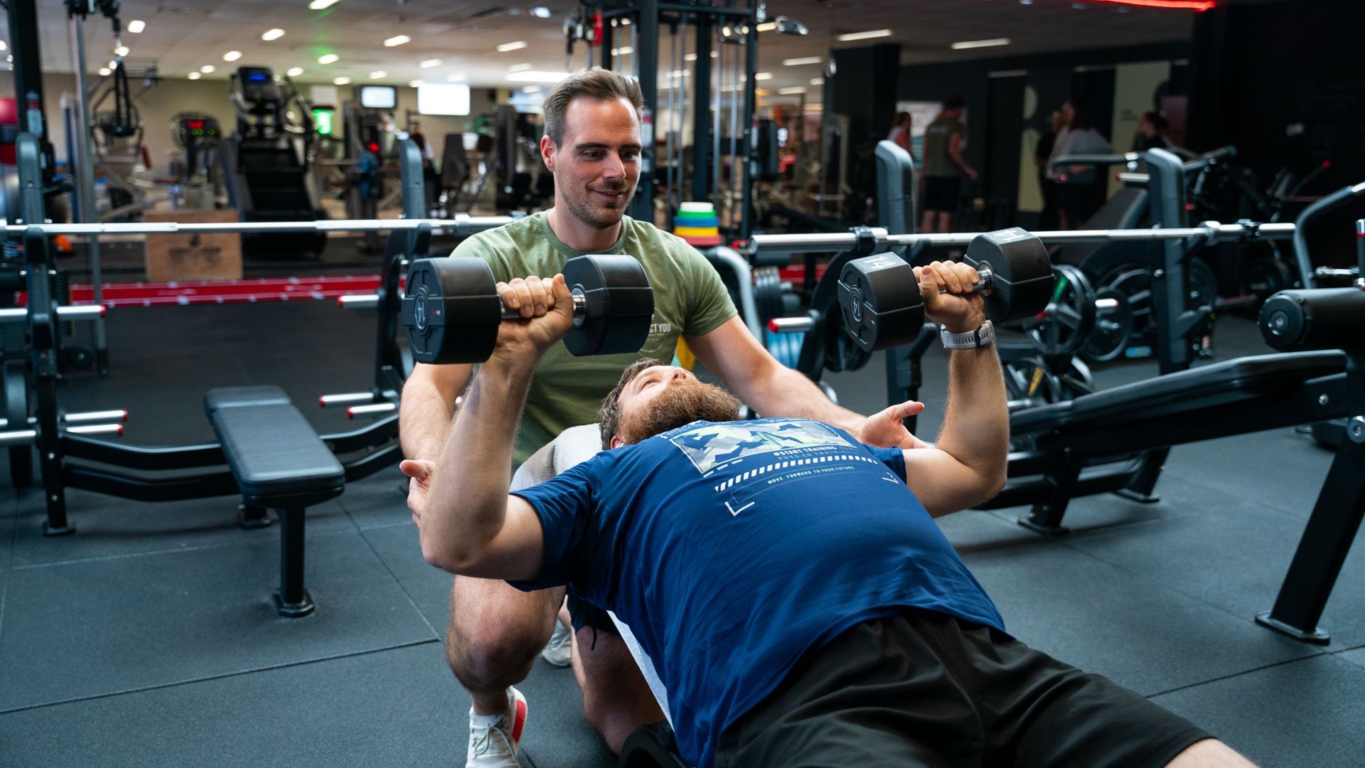 Een man tilt halters op een bankje in een sportschool.