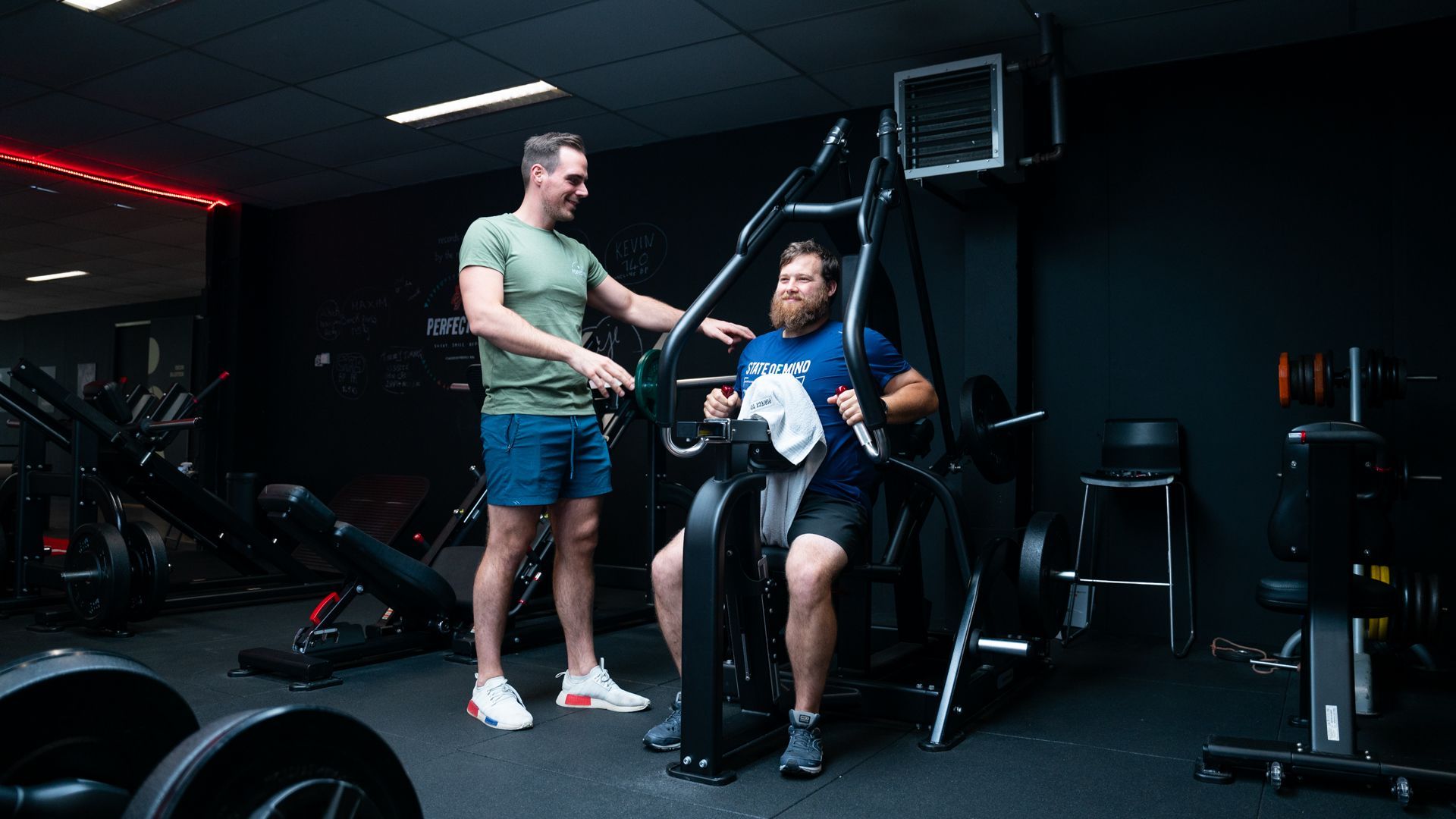 Een man praat met een andere man terwijl hij op een machine in een sportschool zit.