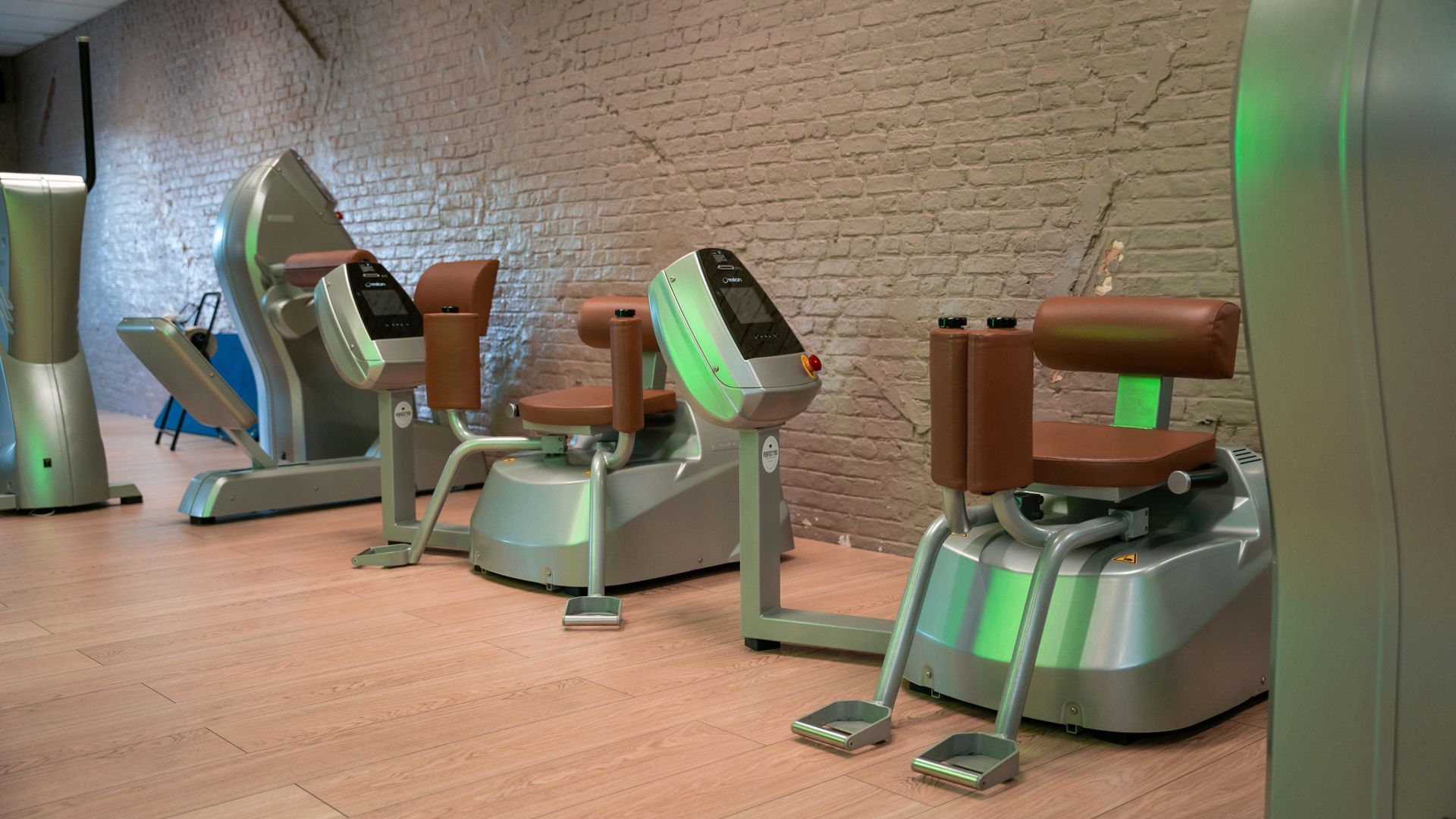 Een rij fitnessapparaten in een sportschool met een bakstenen muur op de achtergrond.