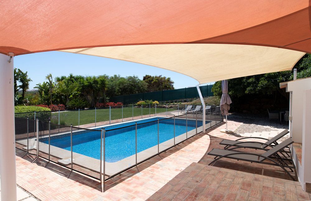 A Large Swimming Pool With A Fence And Chairs Under A Canopy — Pool Installation in Newcastle, NSW