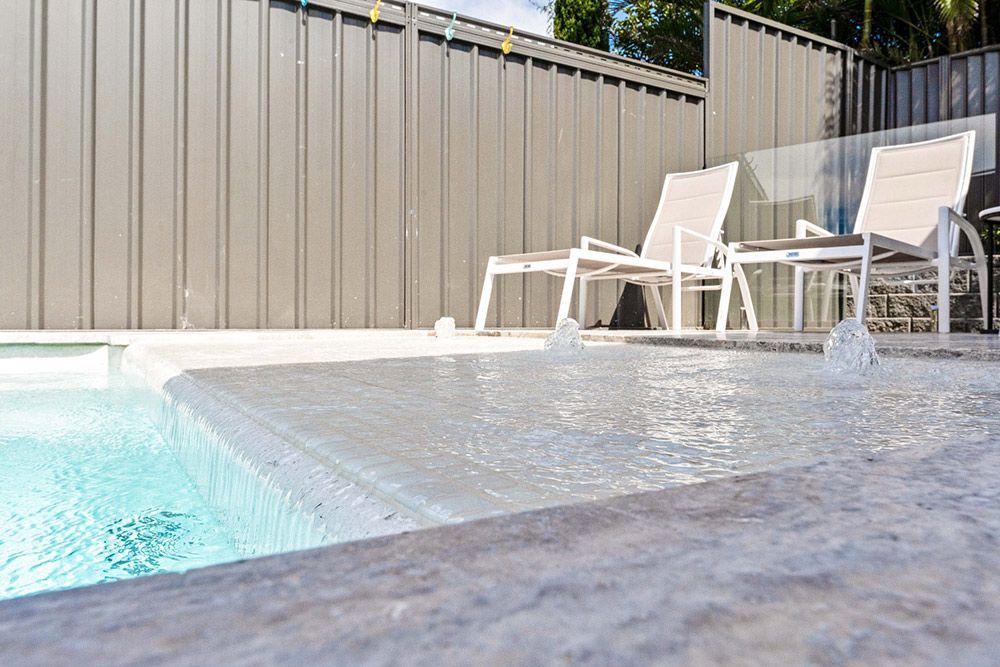 A Swimming Pool With Chairs And A Fence In The Background — Fibreglass Pools in Newcastle, NSW