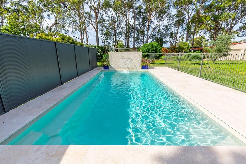 A Large Swimming Pool Surrounded By Trees And A Fence — Fibreglass Pools in Newcastle, NSW