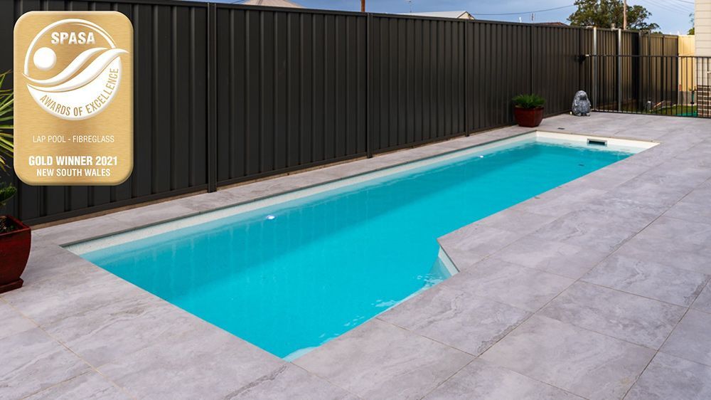 A Large Swimming Pool Is Surrounded By A Black Fence — Fibreglass Pools in Newcastle, NSW