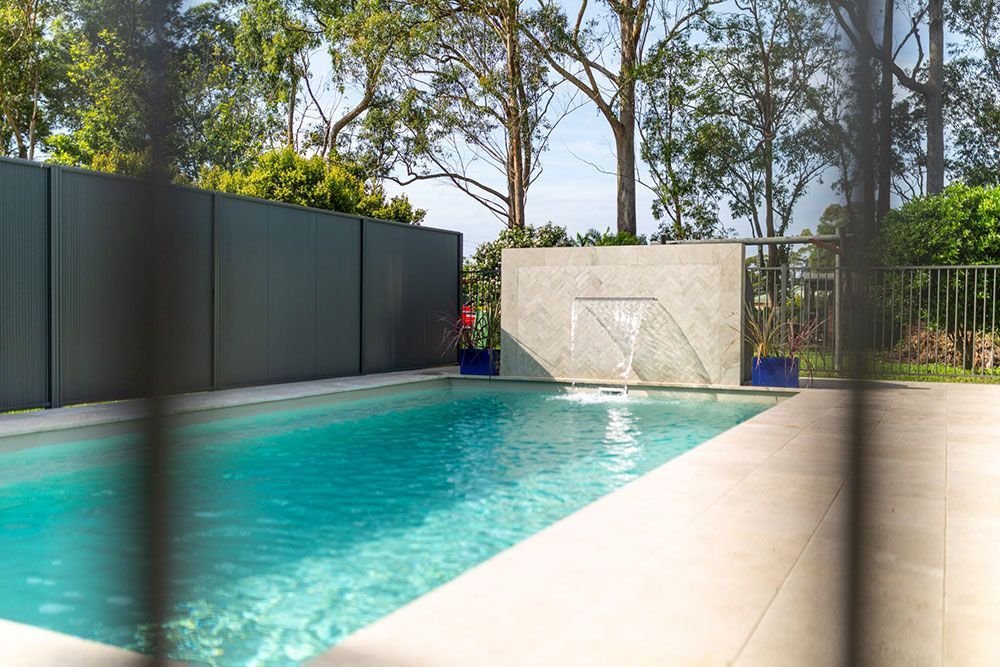 A Large Swimming Pool With A Waterfall In The Backyard Behind A Fence — Pool Installation in Newcastle, NSW