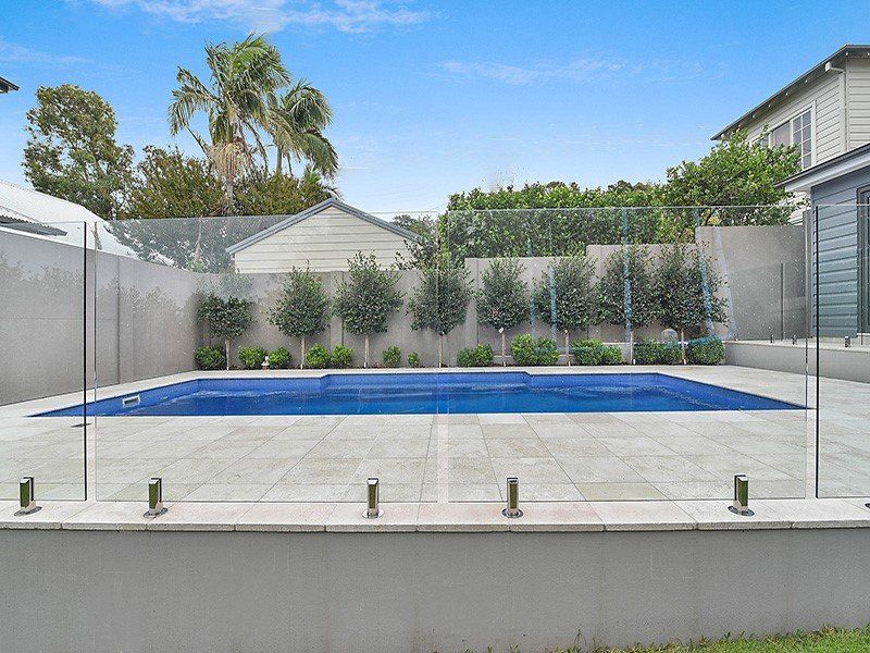 A Large Swimming Pool Is Surrounded By A Glass Fence — Pool Installation in Newcastle, NSW