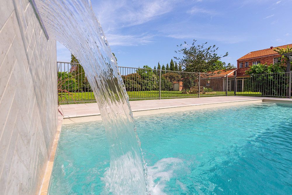 A Waterfall Is Coming Down The Side Of A Swimming Pool — Pool Installation in Newcastle, NSW