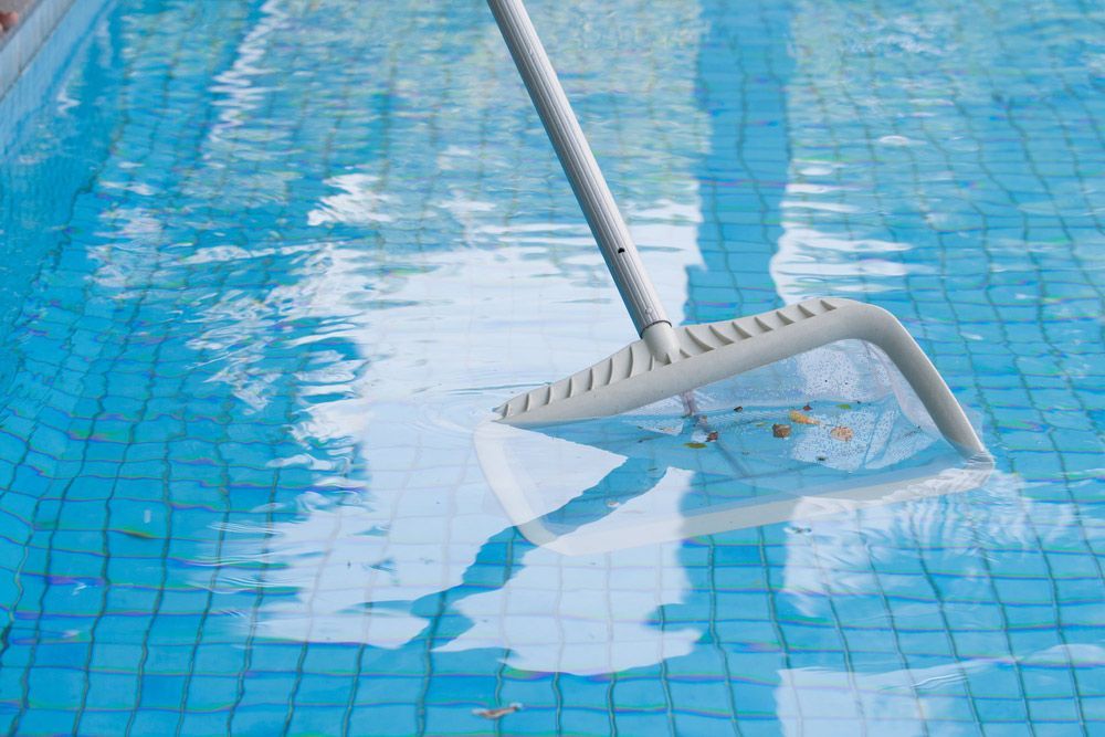 A Broom Is Being Used To Clean A Swimming Pool — Automatic Pool Cleaner in Newcastle, NSW
