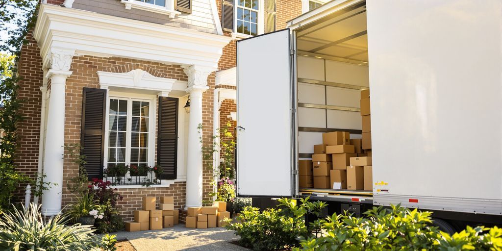 Two movers loading a cardboard box into a truck parked in front of a house.