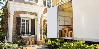 Two movers loading a cardboard box into a truck parked in front of a house.