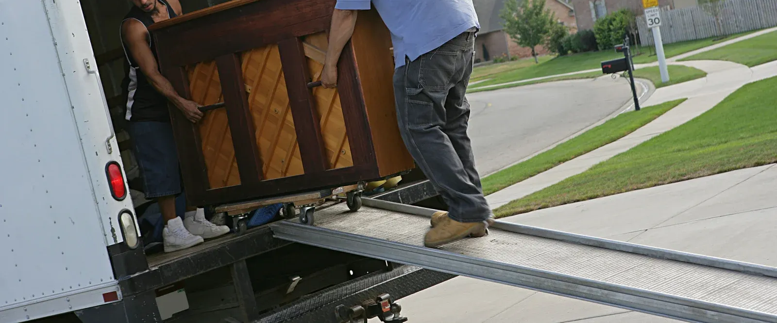 Two people loading a piano onto a truck using a ramp on a sunny day.