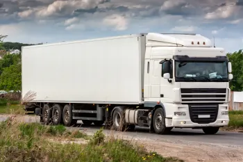 White semi-truck on a dirt road, cloudy sky in the background.