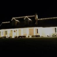 Brightly lit two-story house at night with white exterior and dormer windows under a dark sky