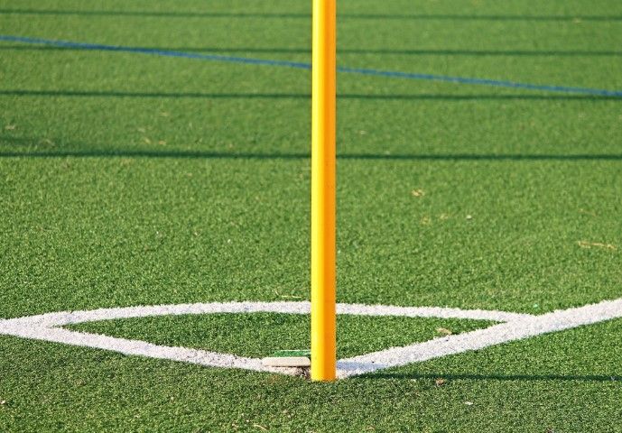A yellow corner flag pole stands on the white corner arc markings of a green artificial turf field.