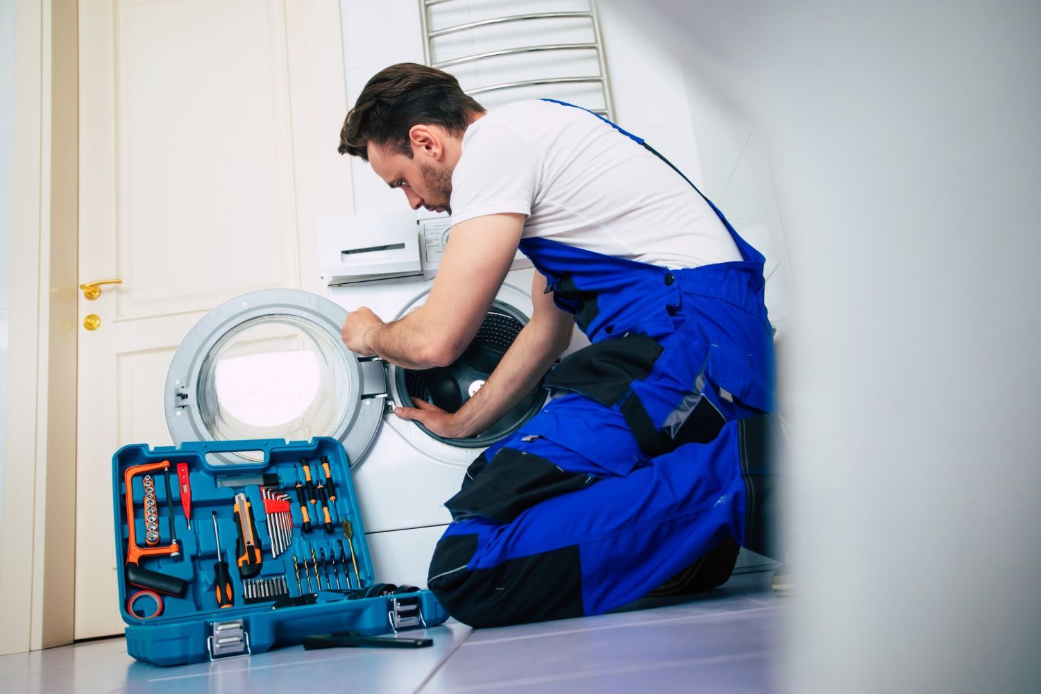 A man is kneeling on the floor fixing a washing machine.
