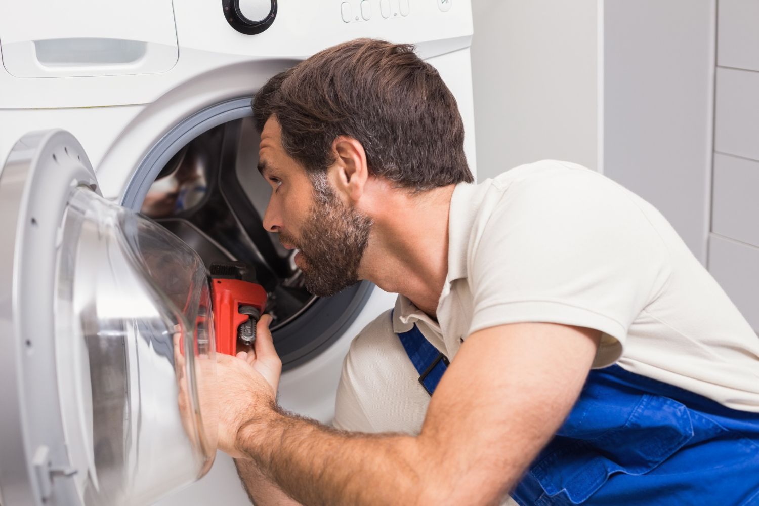 A man is fixing a washing machine with a wrench.