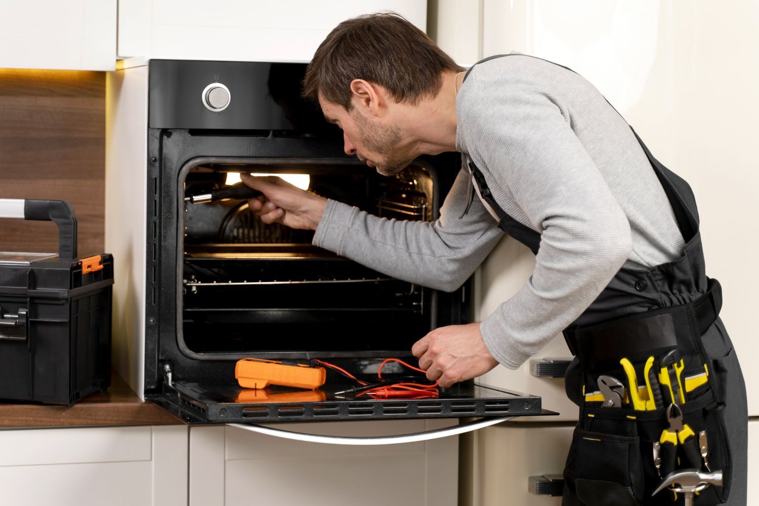 A man is fixing an oven in a kitchen.