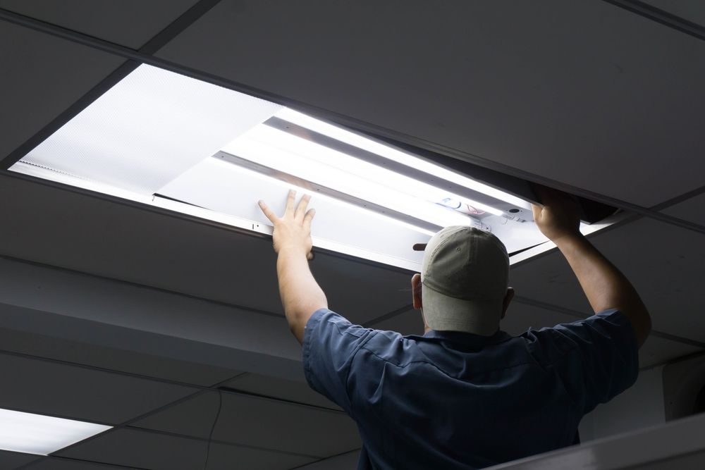 Person in Blue Shirt Replacing Fluorescent Light Fixture in a Drop Ceiling — Rohr Electrical in Wellington, NSW