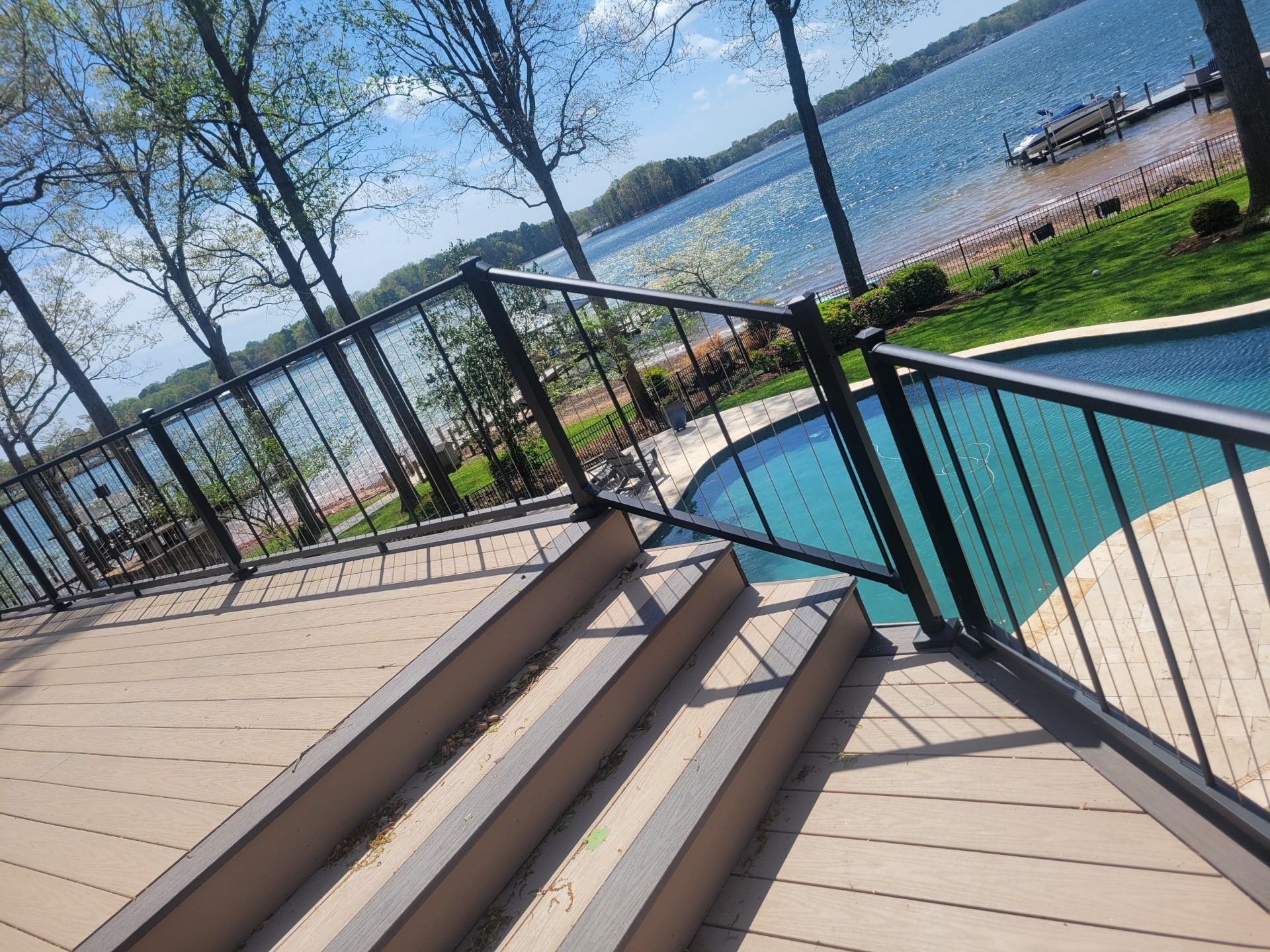 Patio steps beside a turquoise pool overlooking a lake and trees on a sunny day
