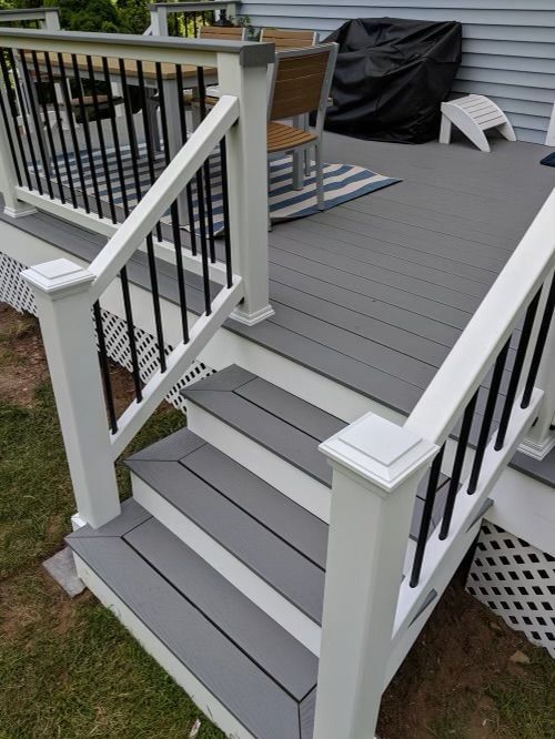 Gray front porch stairs with white railings and black balusters leading to a deck.