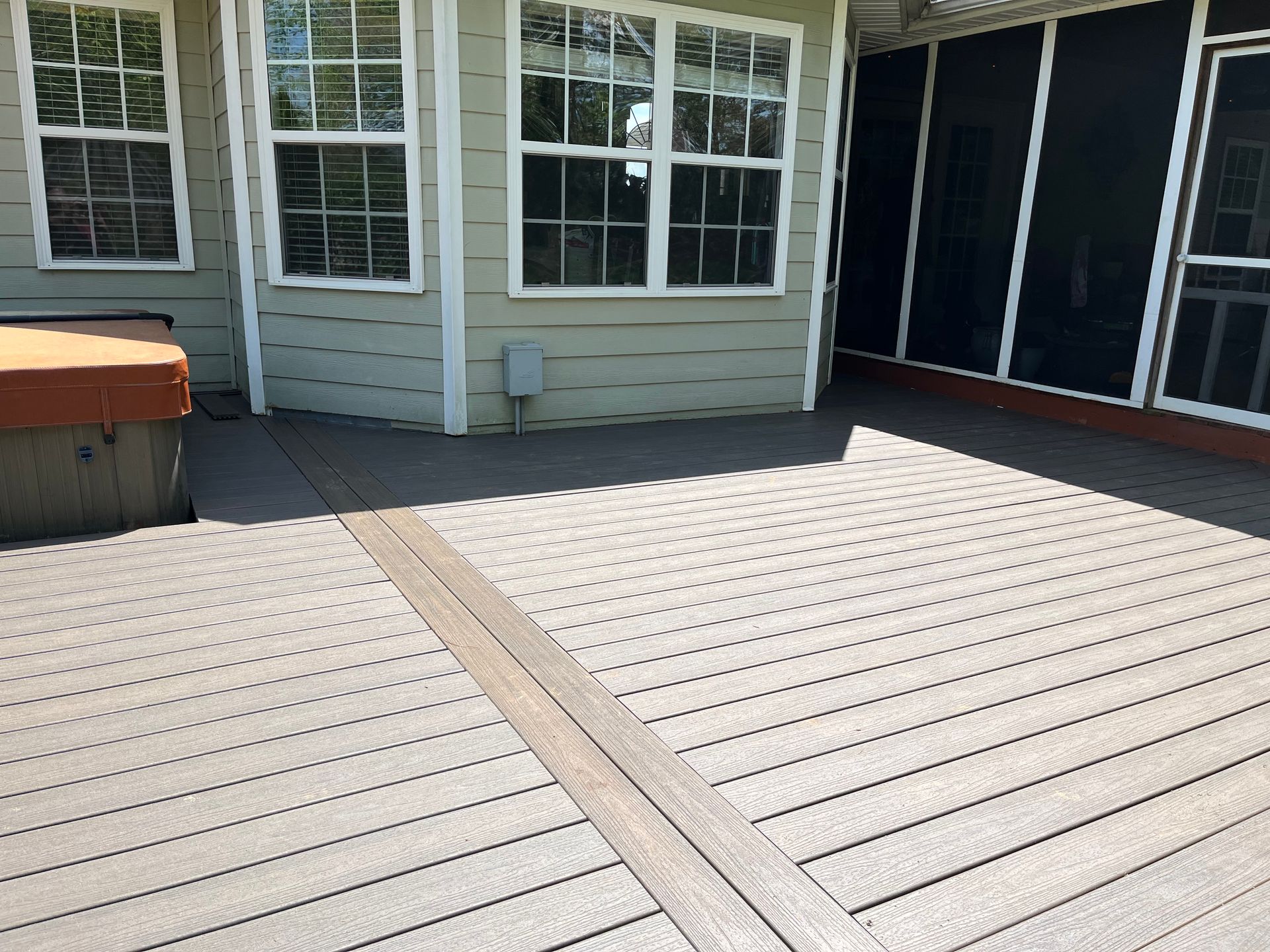 Sunny backyard deck with gray boards, sliding glass doors, and windows on the house exterior