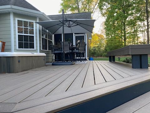 Backyard deck with gray patio furniture, large umbrella, and wooded yard at sunset