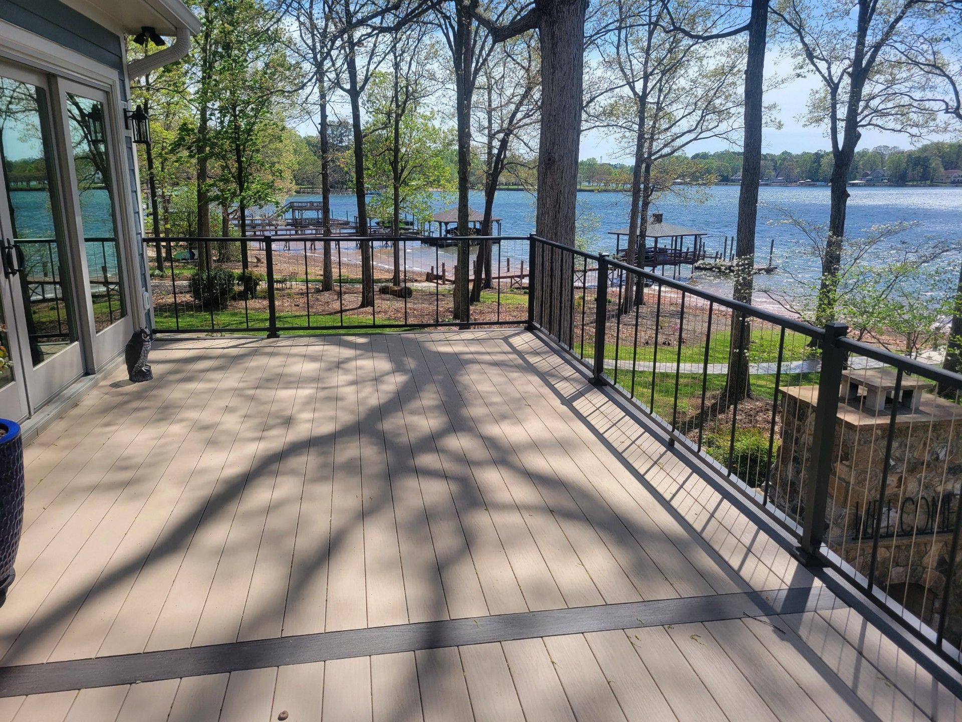 Wooden deck overlooking a lake, with black railings and trees in bright daylight.