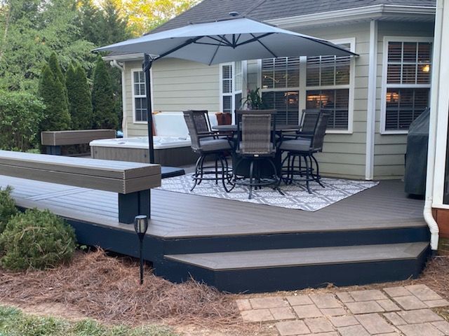 Back patio with umbrella-covered dining set, dark deck, and steps leading to a paved path