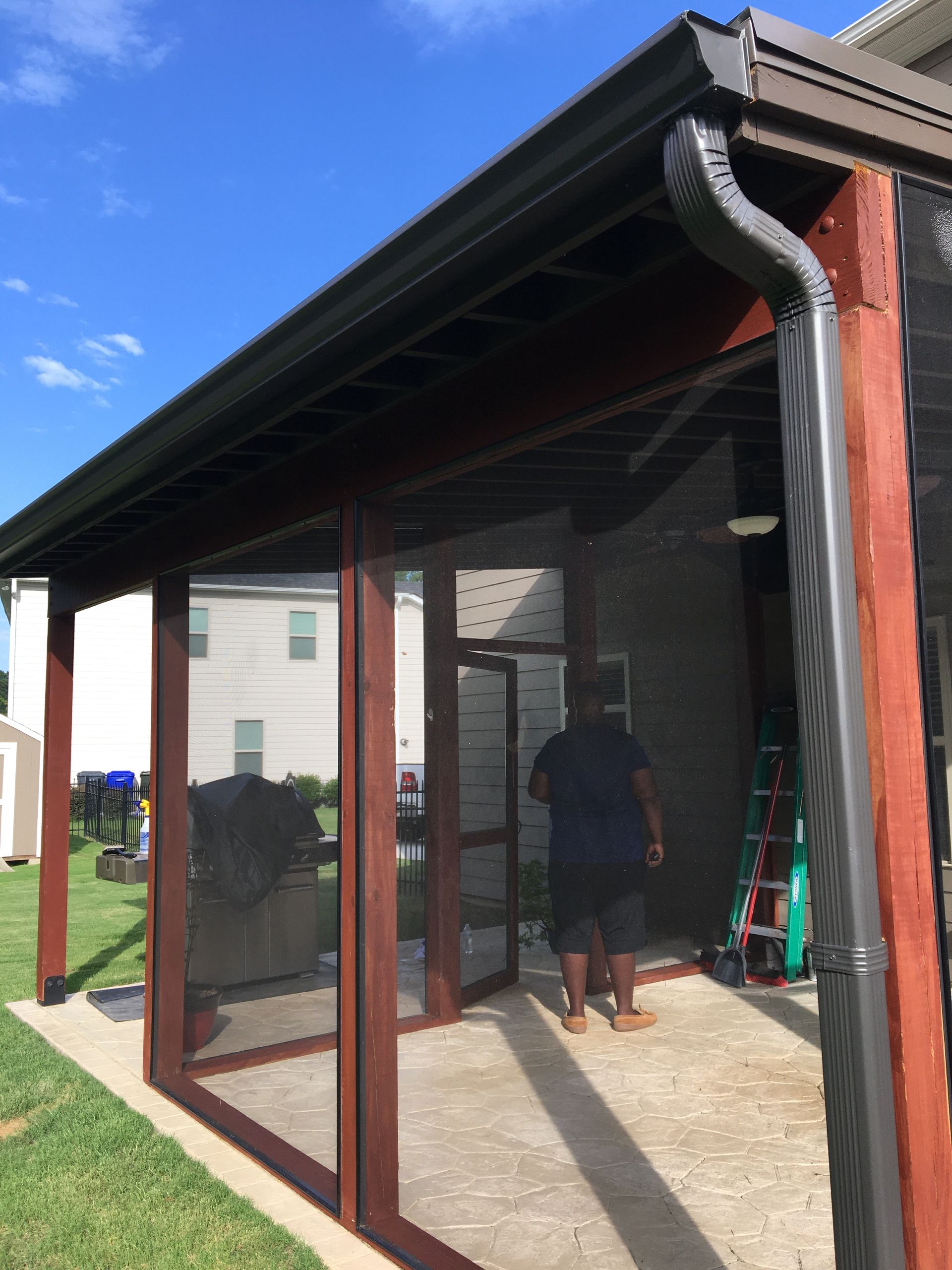 Screened porch with dark roof and red posts; a person stands inside near the doorway.