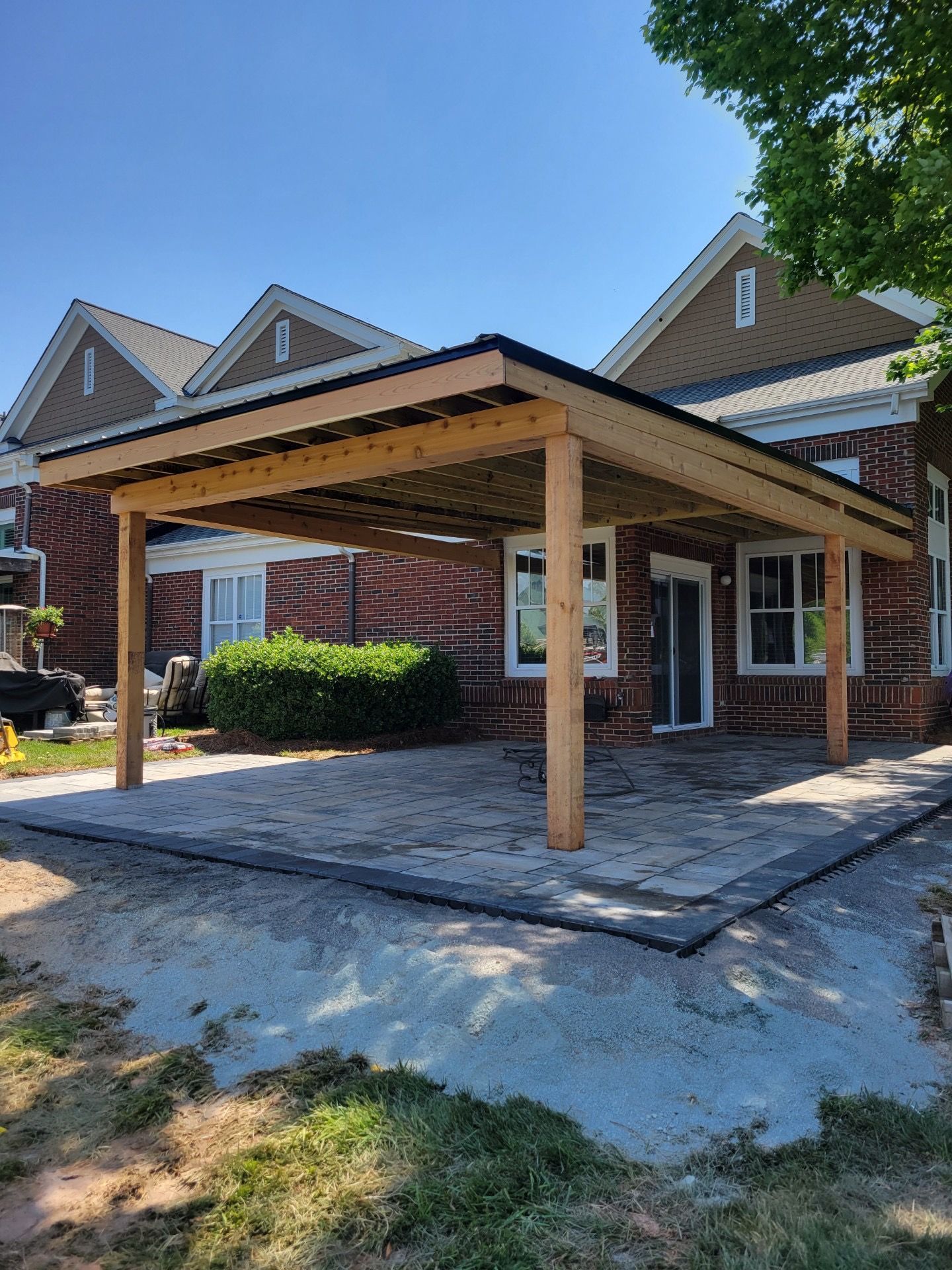 Brick house with a wooden carport under construction and a gravel driveway in front