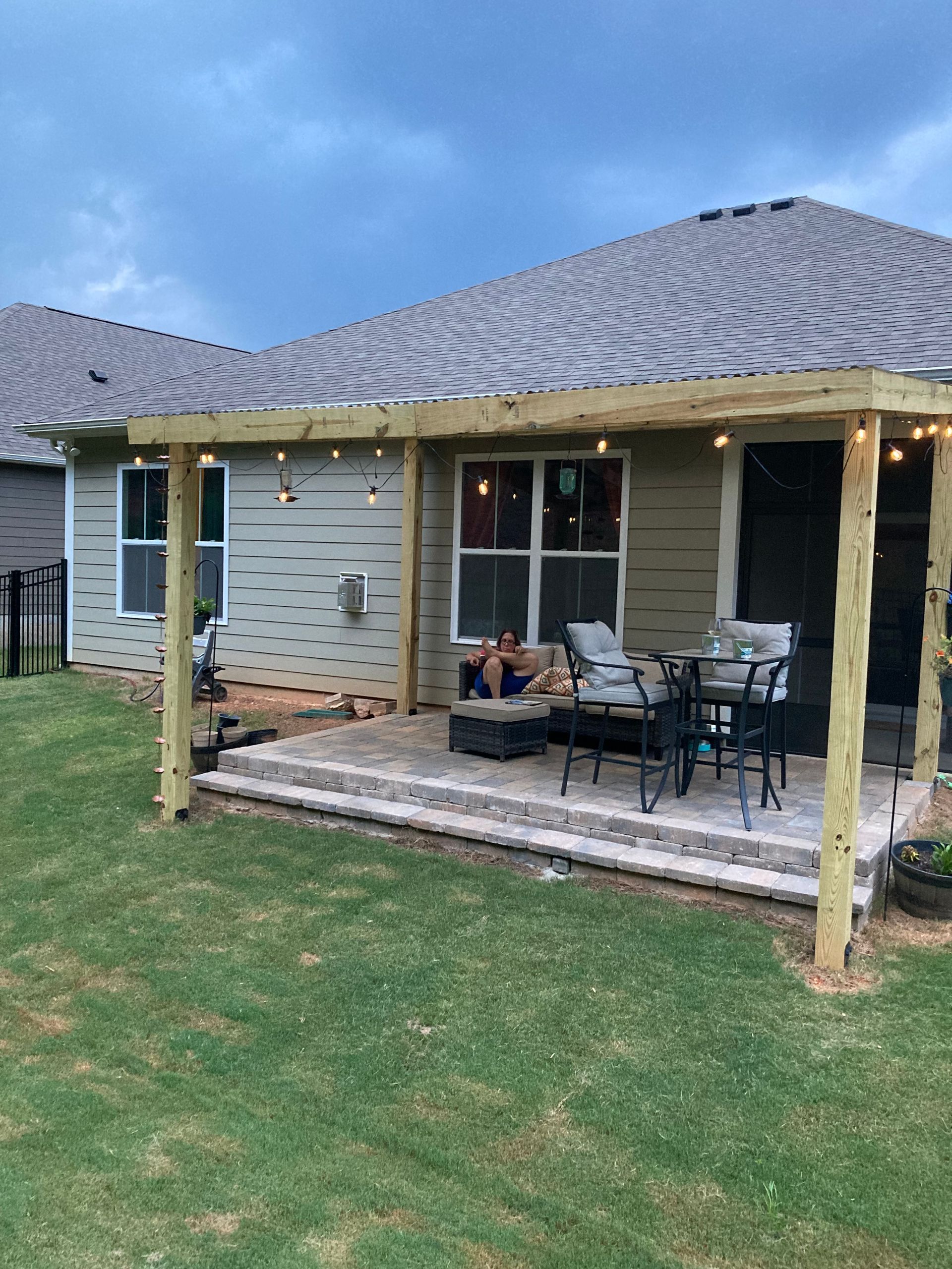 Backyard patio with covered porch, outdoor table and chairs, and a lawn beneath a cloudy sky.