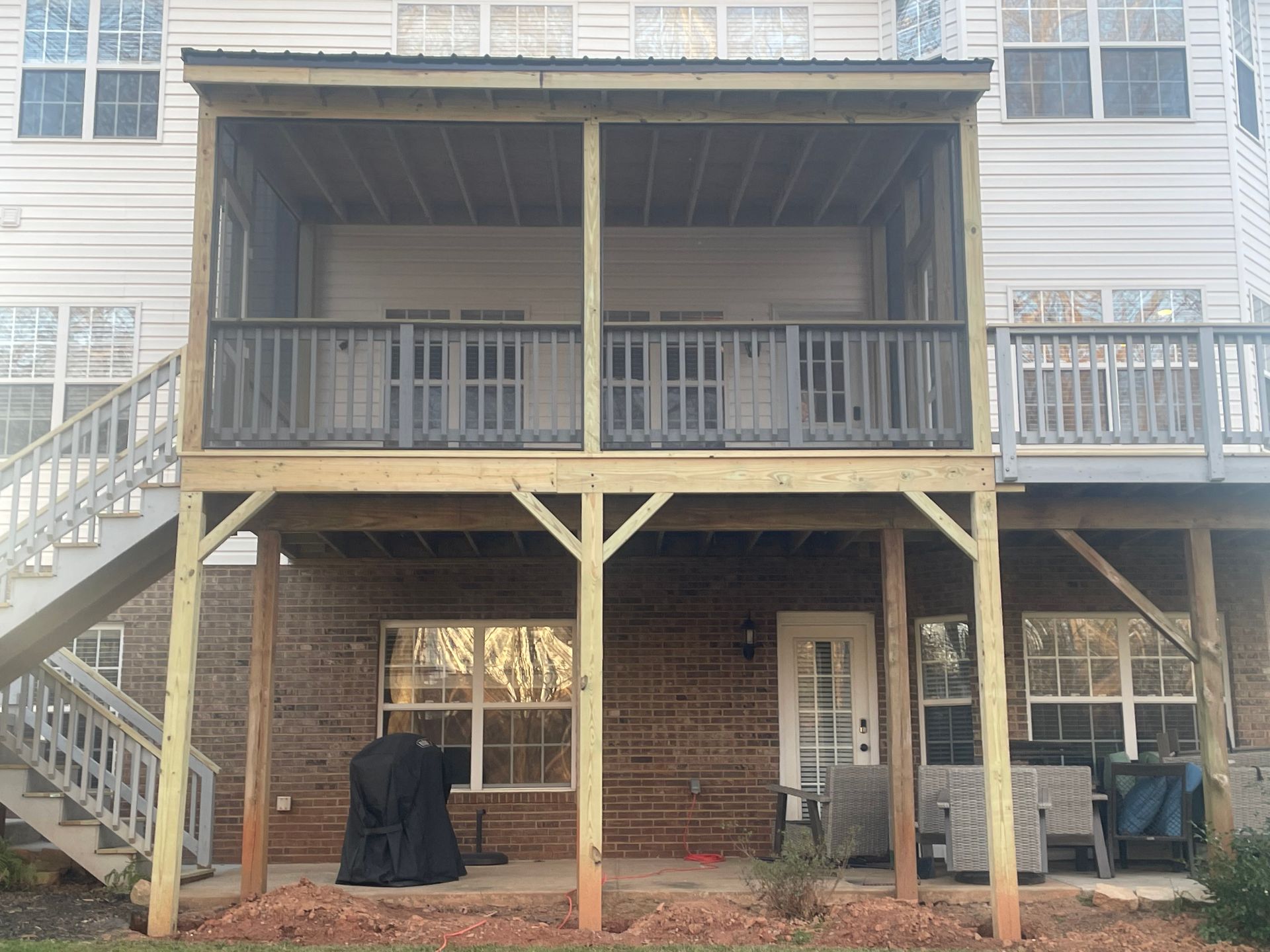 Back deck and stairs on a brick-and-siding house, with a covered patio and railing.