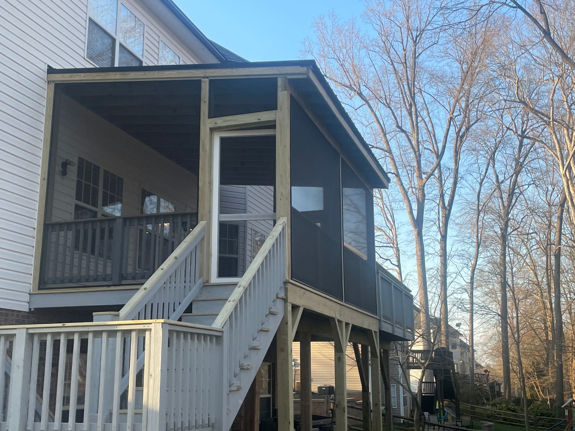 White house side porch with stairs, railing, and screened enclosure in a wooded yard
