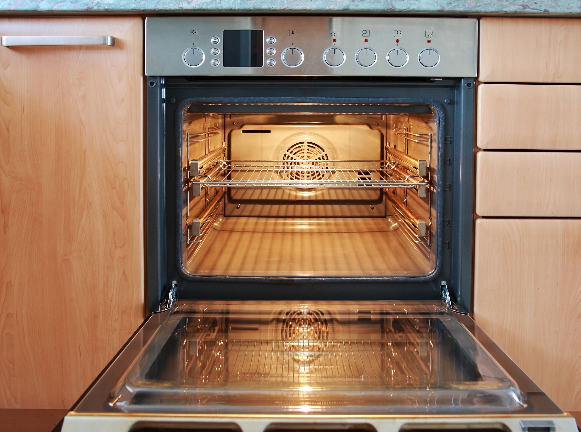 Open kitchen oven with lit interior and stainless steel control panel, door open downward
