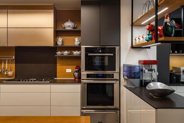 Modern kitchen with dark countertops, beige cabinetry, built-in ovens, and shelves with dishes and decor