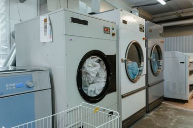 Industrial laundry machines in a clean utility room, with front-loading washers and dryers.